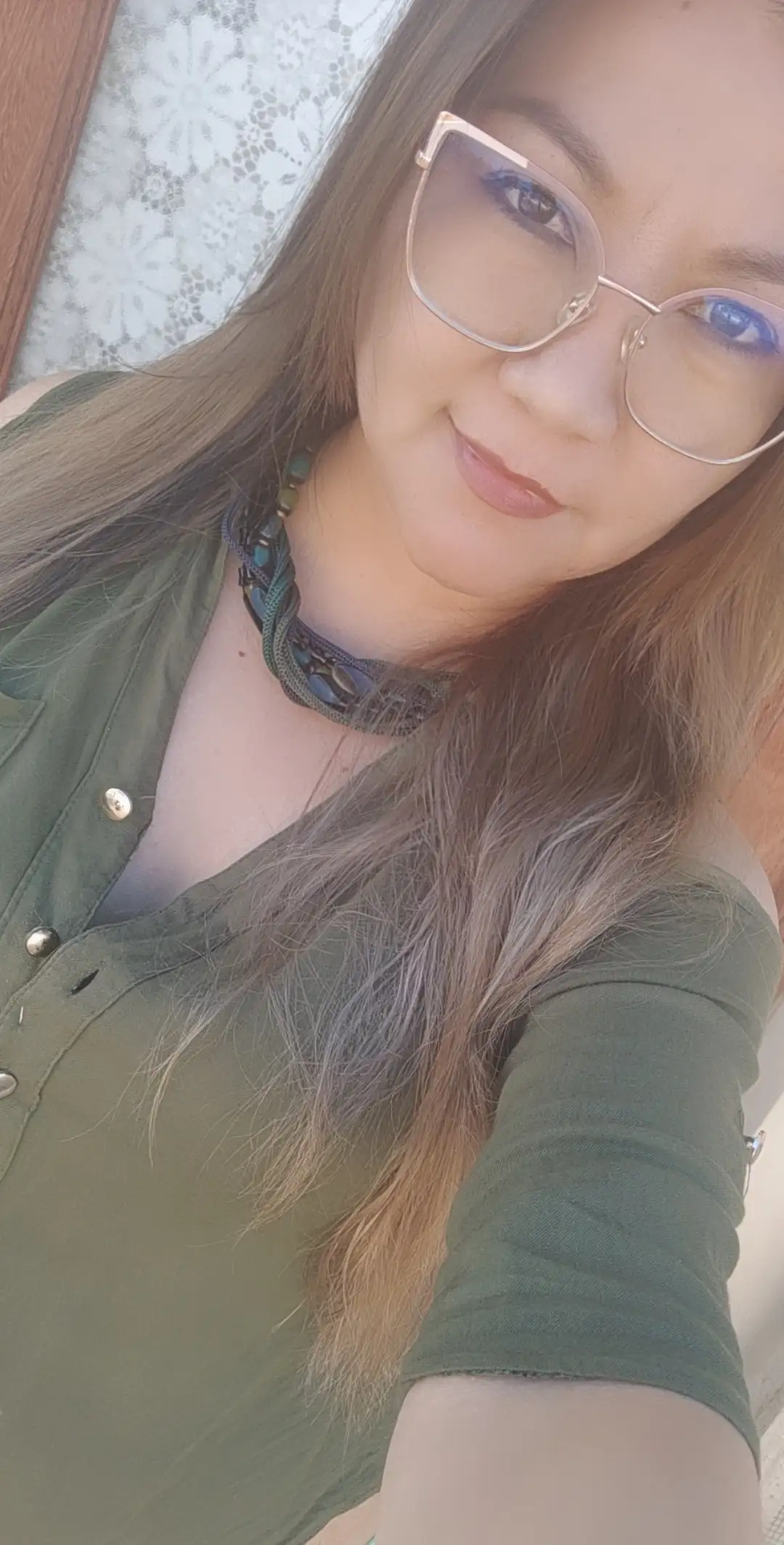 Usando mi foto, una glamurosa mujer de cabello castaño largo y liso posa con seguridad sobre un fondo de estudio neutro. Lleva un blazer negro de corte profundo sin camisa, con un estilo atrevido y elegante. Su maquillaje es impactante, con una piel impecable, delineador de ojos definido y labial rojo oscuro. Complementa su imagen con delicadas joyas de plata: un collar fino con un colgante, una pulsera y un anillo. Su expresión es feroz y segura, irradiando sofisticación y poder. Fotografía de moda profesional, alta resolución, iluminación de estudio suave, estilo editorial.