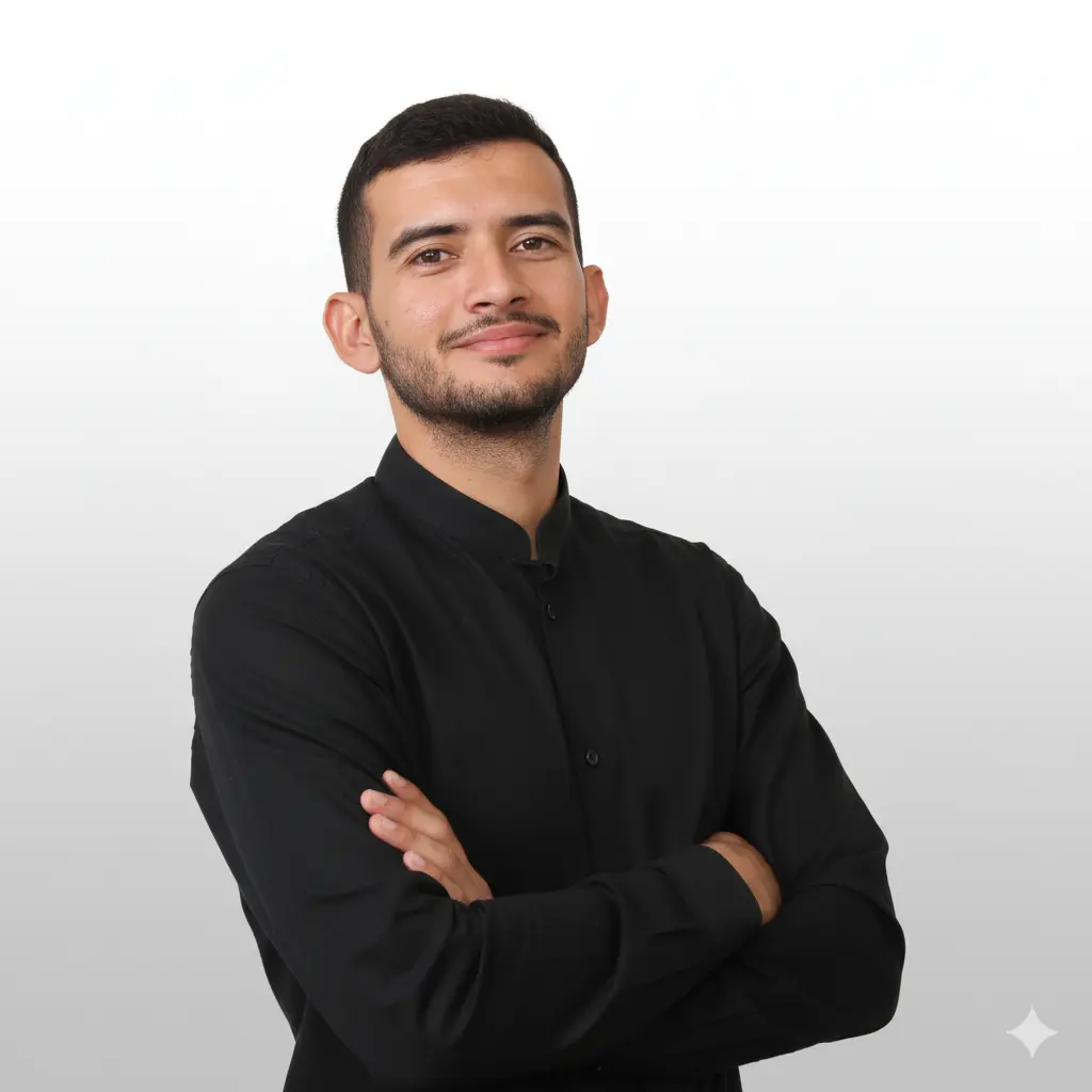 Genera una foto, el hombre joven con barba muy corta y cabello oscuro, vistiendo una camisa negra de cuello mao con los brazos cruzados. Tiene una expresión amable y mira directamente a la cámara. El fondo es un degradado suave de blanco a gris claro.